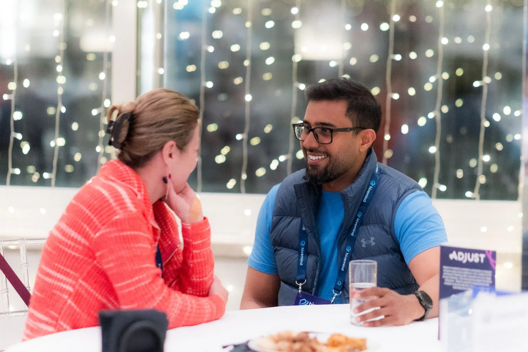 Dhee laughing in conversation across a dinner table under fairy lights.